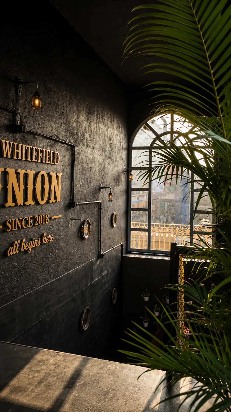Whitefield Union bar, Bangalore — brass lettering and reclaimed gears on the black entry wall, lit by caged pipe lights