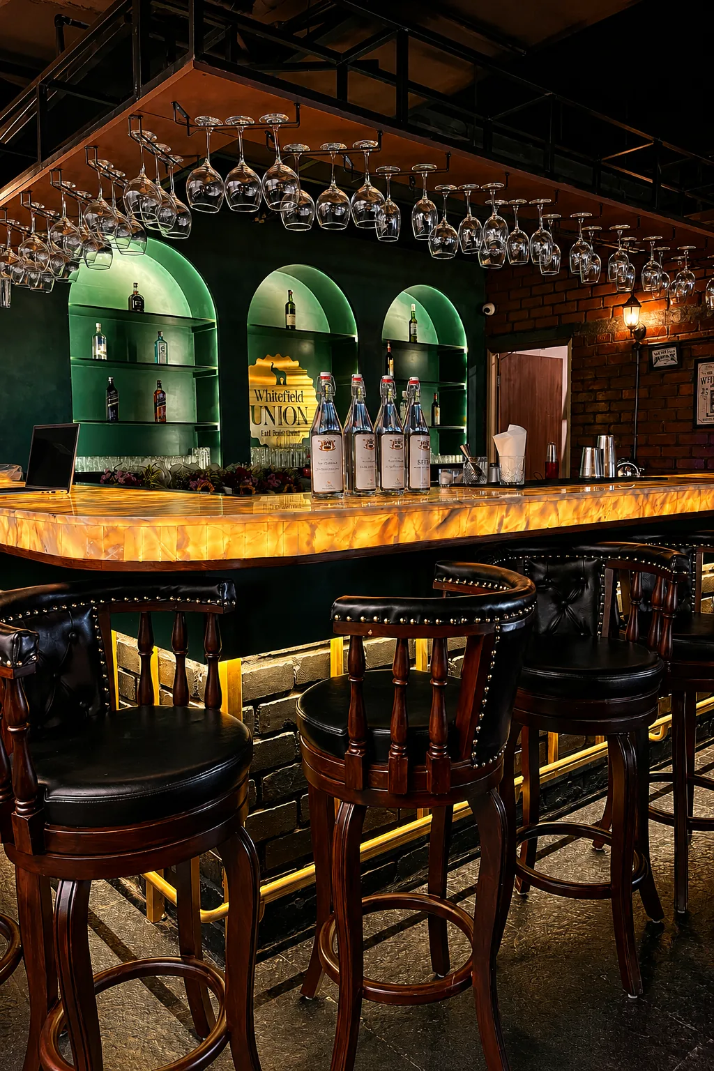 Whitefield Union bar, Bangalore — backlit onyx counter and green arched liquor niches under hanging glassware